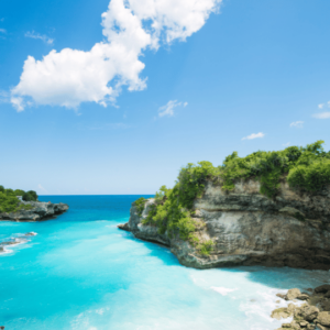 The image shows a beautiful blue lagoon in Bali, Indonesia. The water is a stunning shade of turquoise and the surrounding cliffs are lush and green. The sky is a clear blue with a few wispy clouds. It's a truly breathtaking scene!